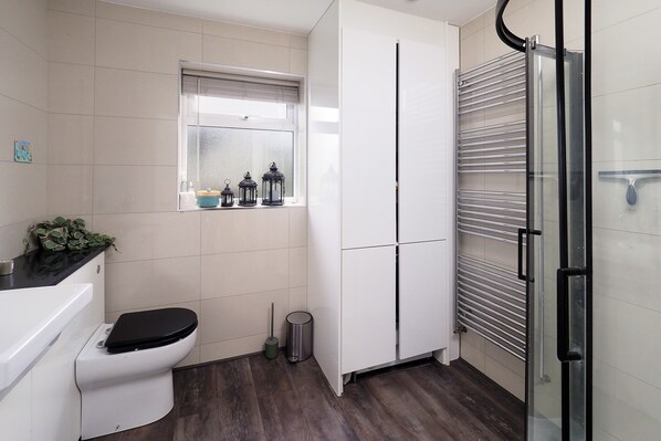 A modern bathroom with a toilet, a window with decorative items, a metal trash bin, and a glass shower enclosure. - Not for rent as using back as own house cannot cancel trying to (Canterbury)