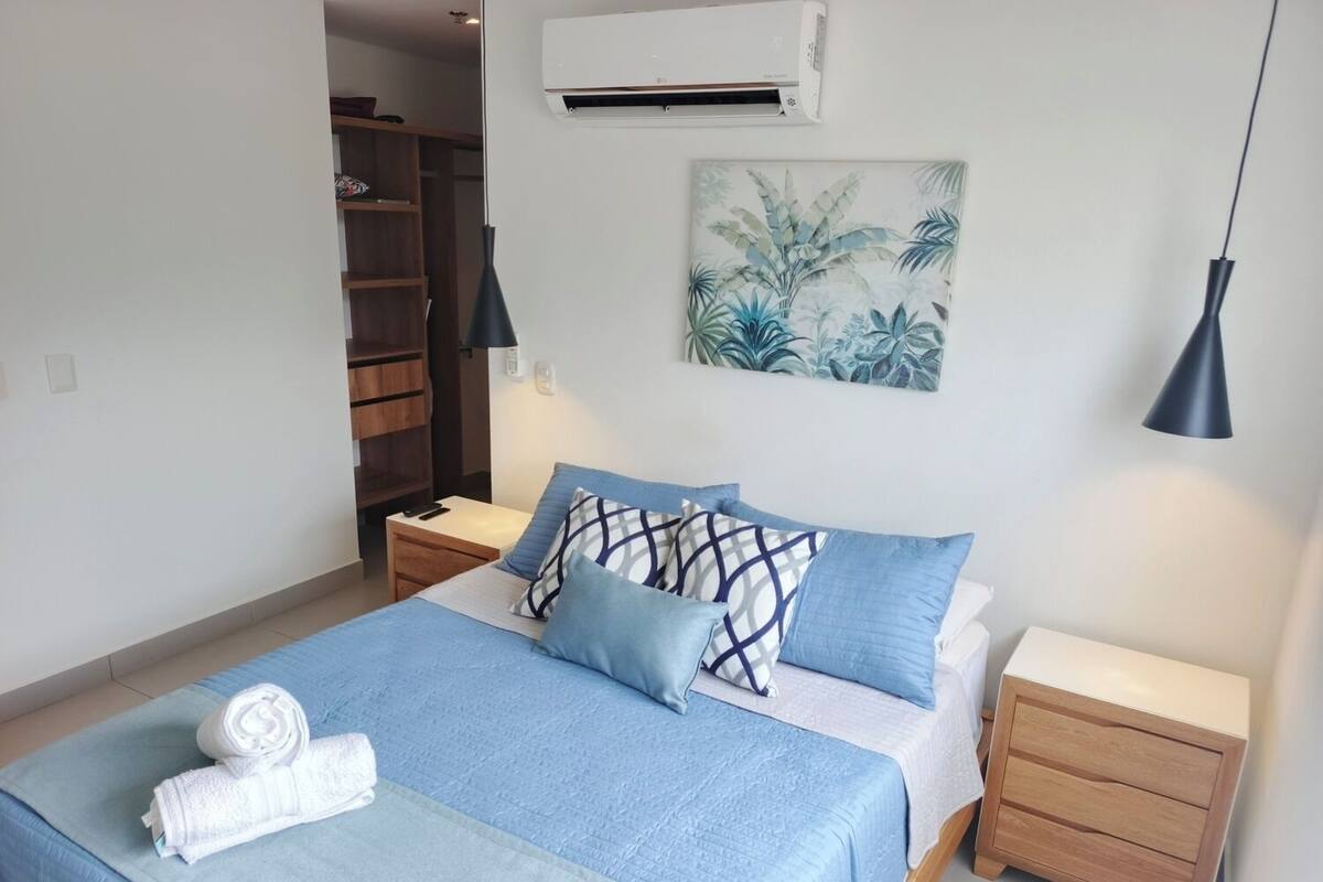 A bedroom with a bed, two bedside tables, a wardrobe, and an air conditioning unit.