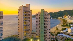A high-rise building with multiple balconies overlooking a beach and ocean. - Apartasuites Ambar Roca - Rodadero (Santa Marta)