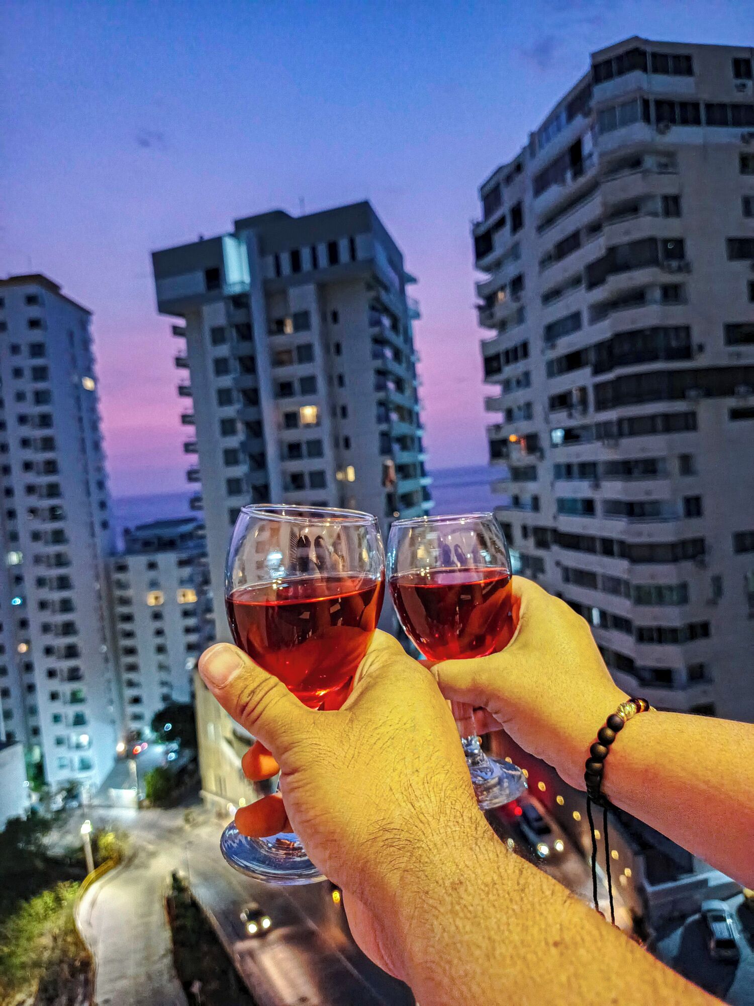 Two hands holding wine glasses with a cityscape in the background.