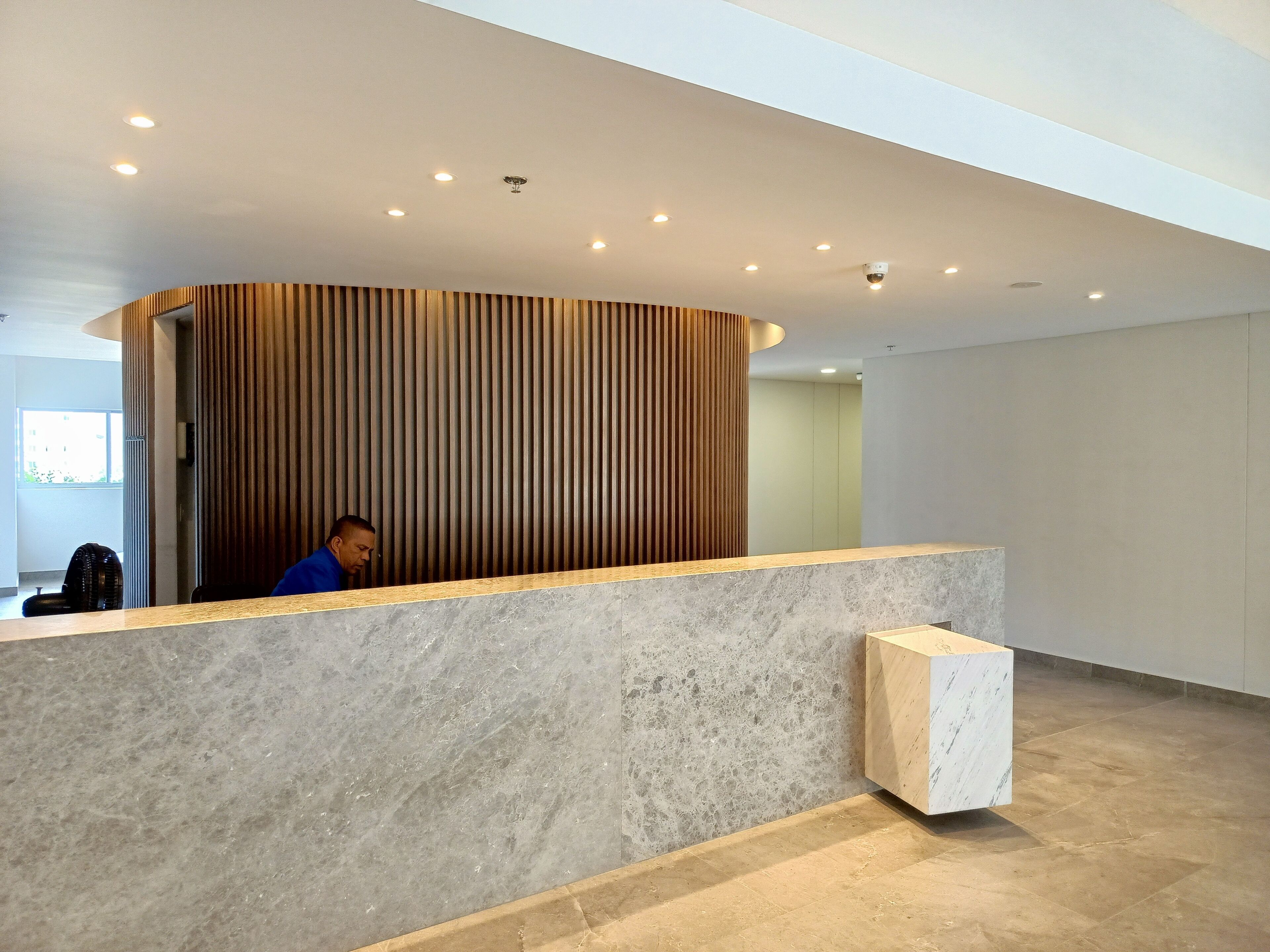 A reception area with a curved wooden panel wall, a marble counter, and a security camera on the ceiling.