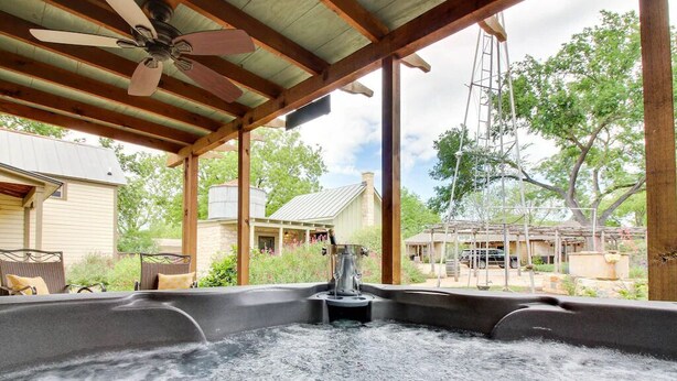 Et område med jacuzzi, loftventilator, træbjælker og udsigt til bygninger og træer i nærheden.