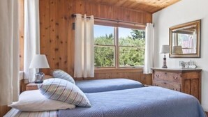 Habitació amb dos llits, parets de fusta, una finestra amb cortines, un taulell i un mirall.