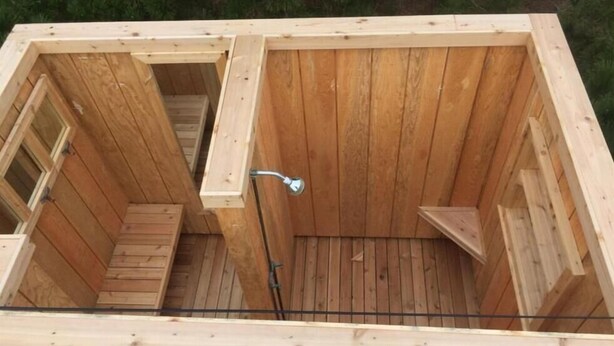Una sauna de fusta amb una banca, una zona de dutxes i una petita finestra.