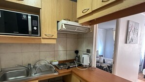 Een compacte keuken met houten kastjes, een magnetron, een broodrooster en een kleine koelkast.