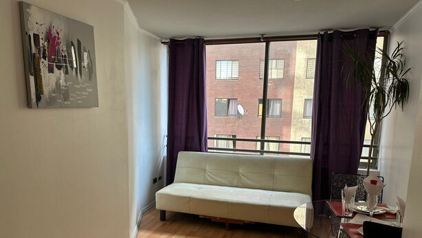 Een woonkamer met een bank, een eettafel met stoelen, een raam met gordijnen en een plant.