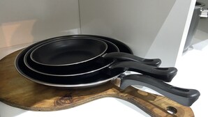 A set of black frying pans on a wooden board with a black handle. - Cares Apartament, Castelar Centro, Buenos Aires. (Castelar)