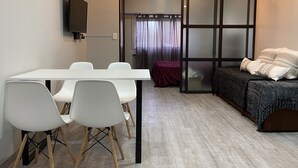 A modern room with a white table and chairs, a dark sofa with patterned cushions, and a sliding glass door leading to a balcony. - Cares Apartament, Castelar Centro, Buenos Aires. (Castelar)
