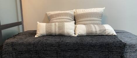 Una cama con una manta gris oscuro y dos almohadas estampadas.