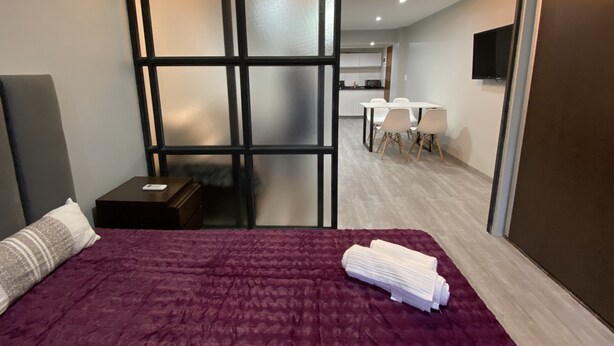 A modern hotel room with a large bed, a desk, and a dining area in the background. - Cares Apartament, Castelar Centro, Buenos Aires. (Castelar)