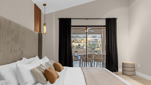 Quarto de hotel moderno com uma cama grande, ventilador de teto e vista para o pátio externo.