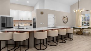 Uma cozinha moderna com uma ilha central, banquetas de bar e uma área de jantar com lustre.