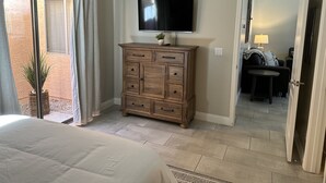 Un dormitorio con una cama, un aparador de madera, un televisor y una puerta corrediza de cristal que da a un patio.