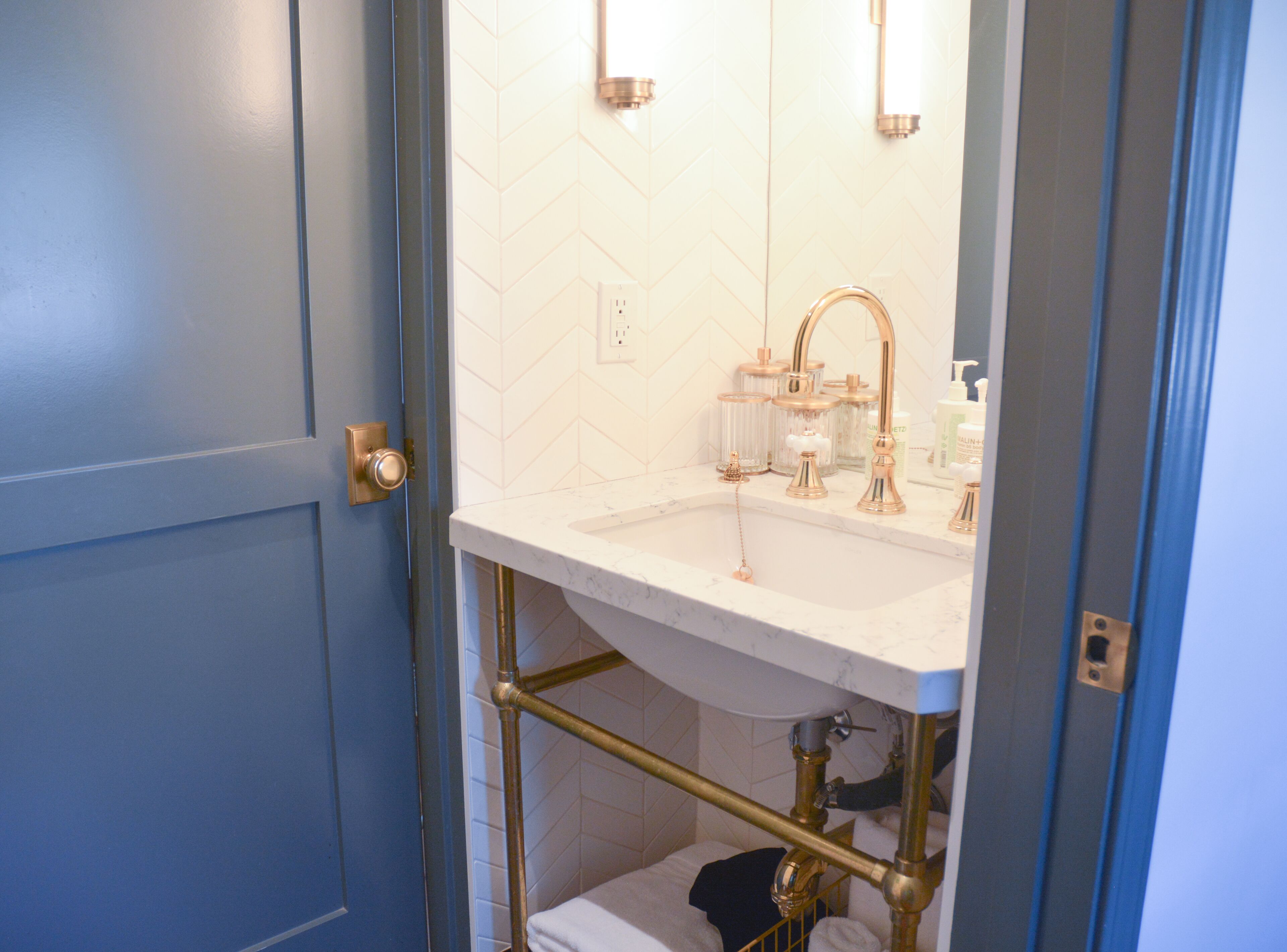 Um banheiro com pia branca, detalhes dourados e porta azul.