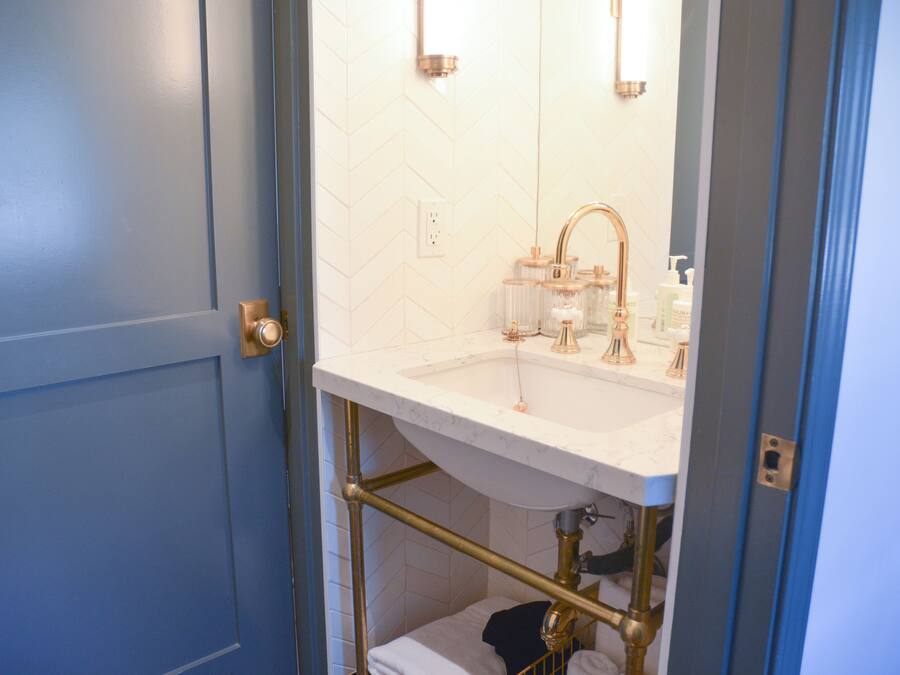 Um banheiro com pia branca, detalhes dourados e porta azul.