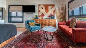 A modern living room with a large red sofa, a blue armchair, a round coffee table, and a patterned rug. - Gold-Diggers Hotel (Los Angeles)