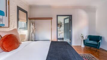 Une chambre à coucher comprenant un lit, une table de chevet, une chaise, un miroir et une porte donnant sur une salle de bain.