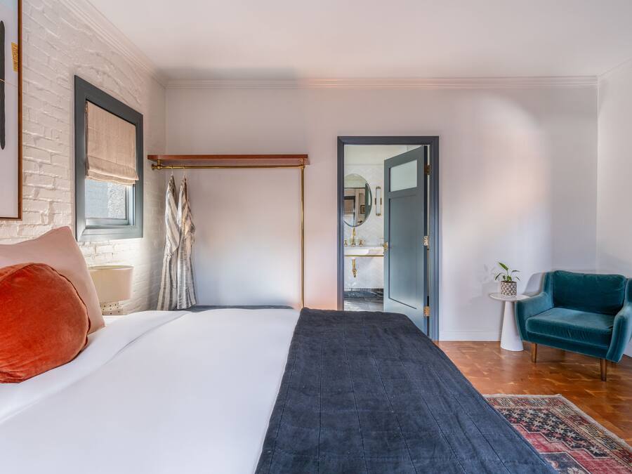 Une chambre à coucher comprenant un lit, une table de chevet, une chaise, un miroir et une porte donnant sur une salle de bain.