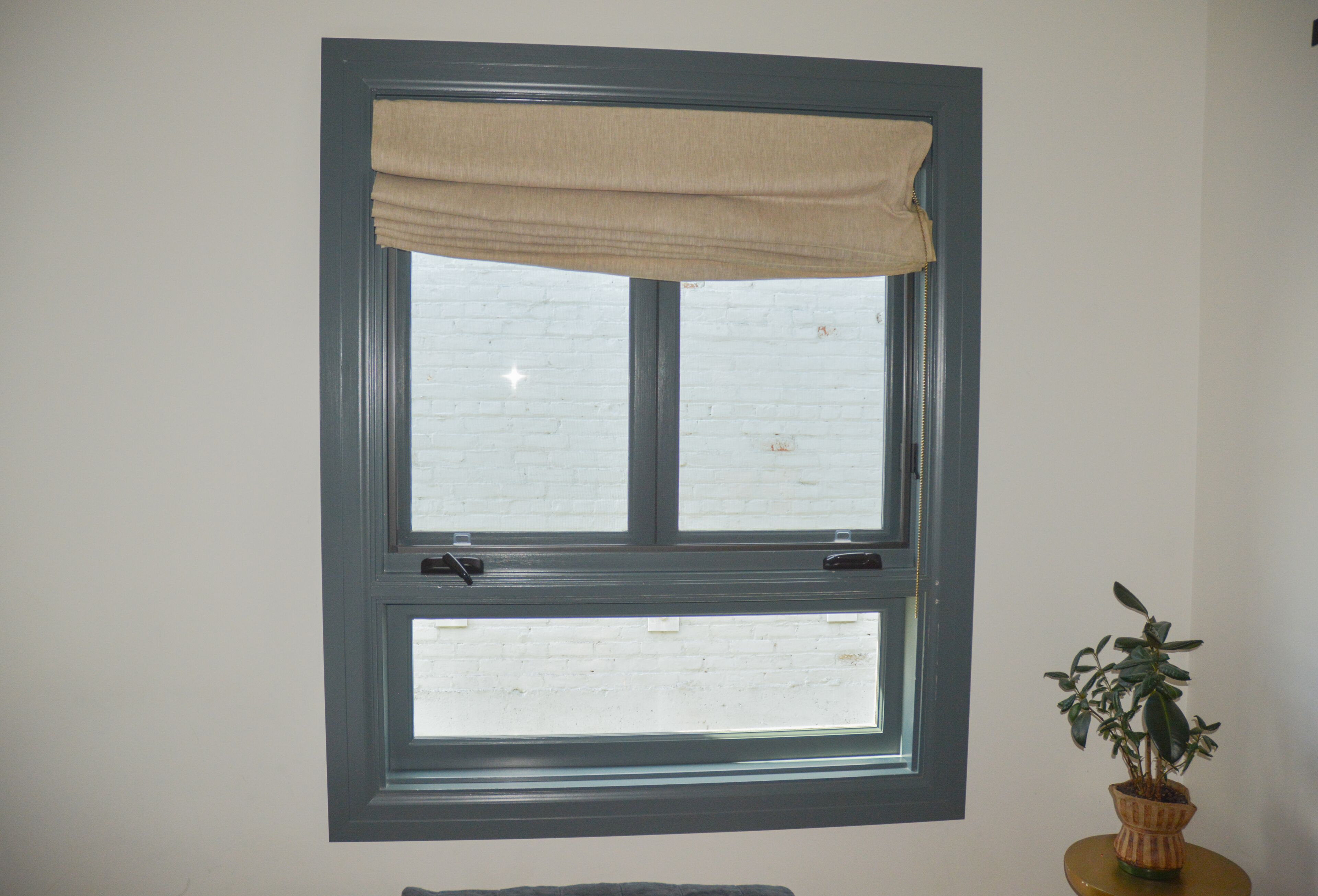 A window with a beige valance and a potted plant on a small table beside it.