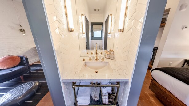 A bathroom with a marble sink, gold fixtures, and a mirror with wall sconces. - Gold-Diggers Hotel (Los Angeles)