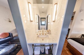 A bathroom with a marble sink, gold fixtures, and a mirror with wall sconces. - Gold-Diggers Hotel (Los Angeles)