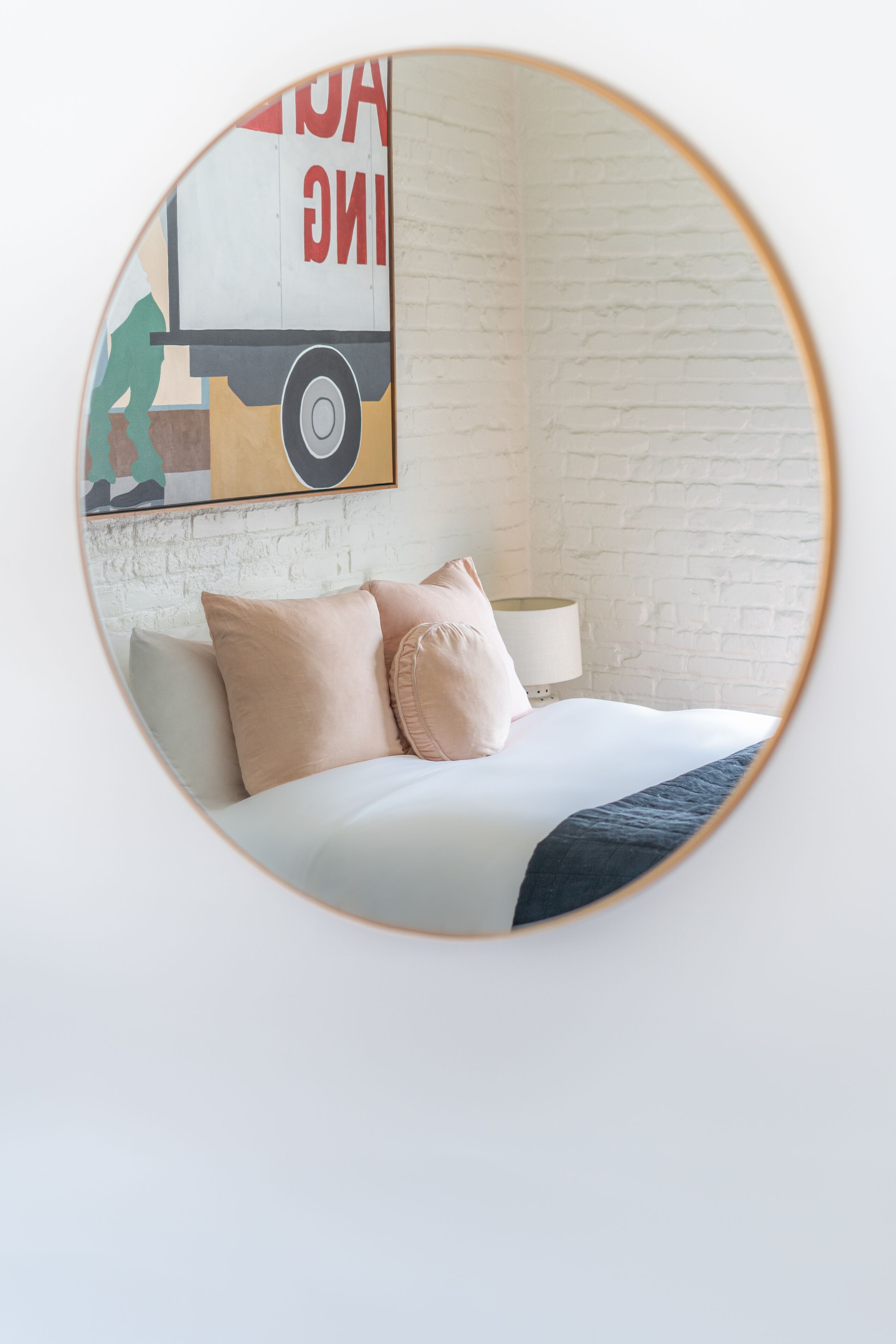 A bedroom with a bed, pillows, a lamp, and a wall with a brick pattern.