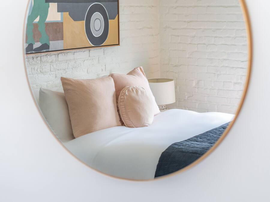 A bedroom with a bed, pillows, a lamp, and a wall with a brick pattern.