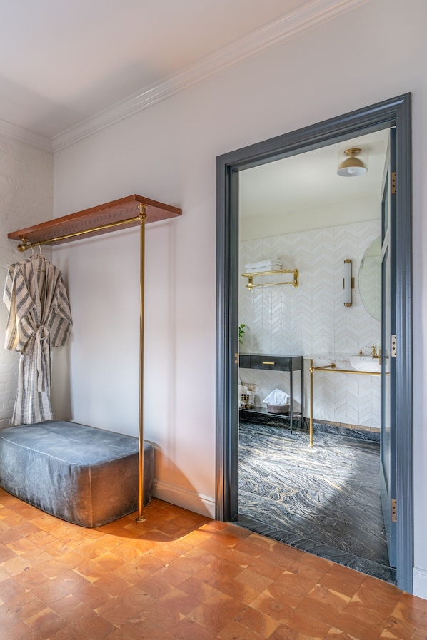Une salle de bain avec un mur recouvert de carreaux disposés en motif chevrons, un banc en bois, un porte-serviettes et un miroir avec un cadre doré.