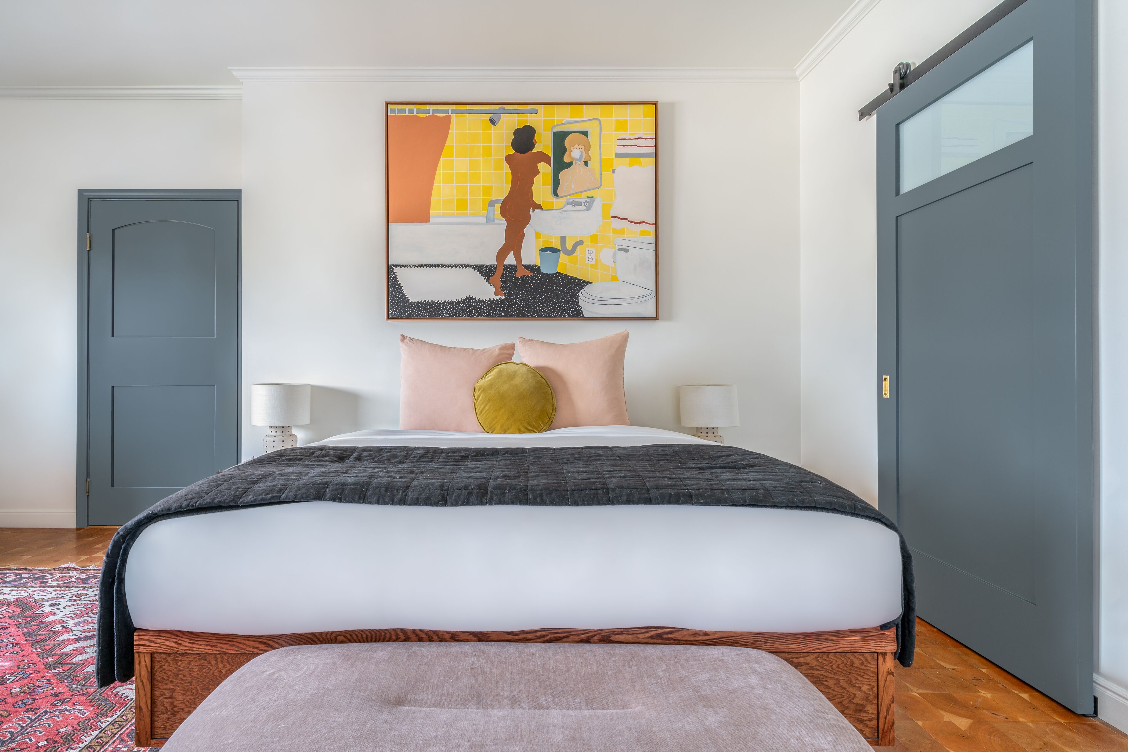 Een slaapkamer met een bed, een schilderij, een deur en een nachtkastje.