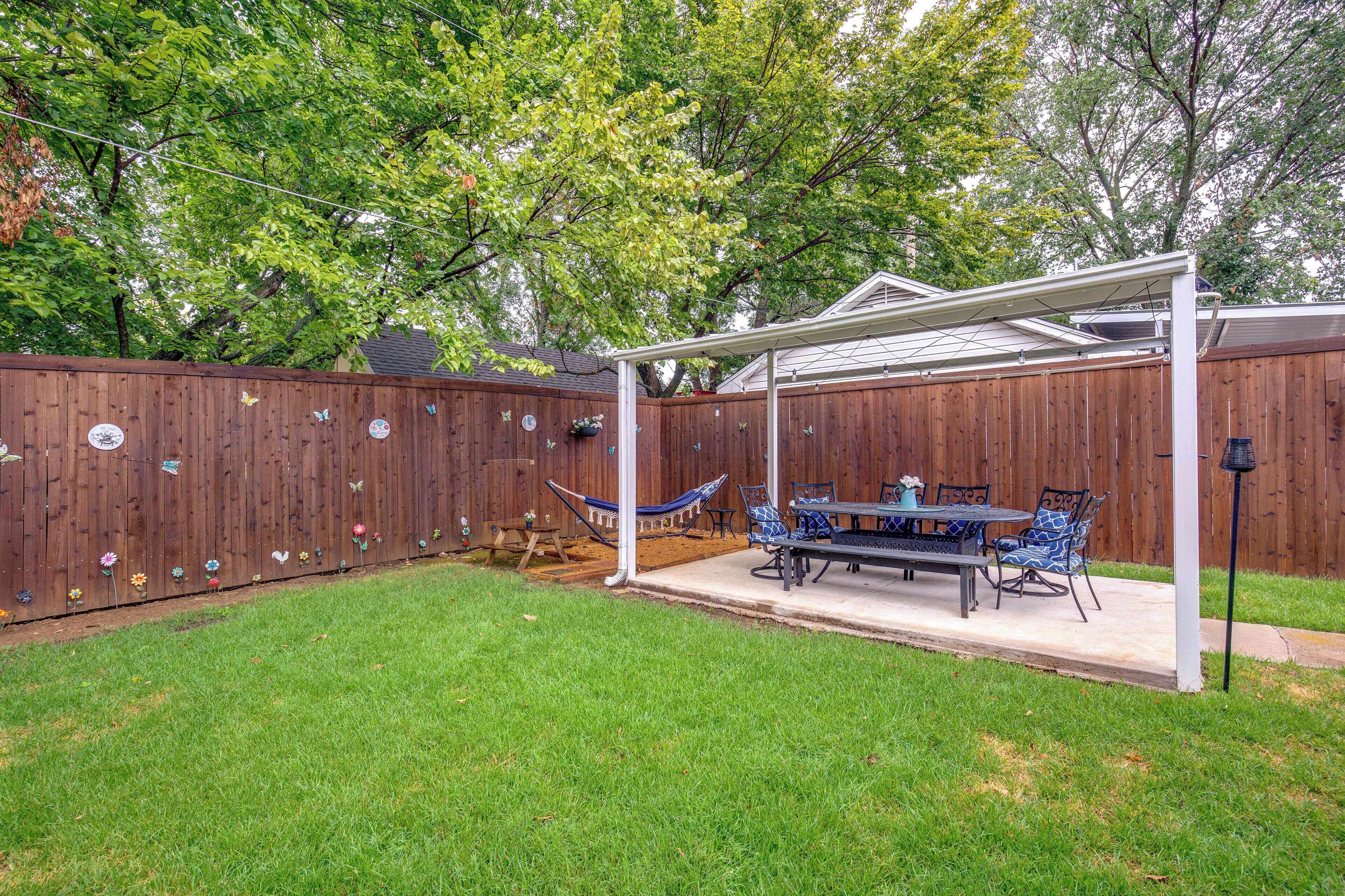 A backyard with a wooden fence, a hammock, a table with chairs, and a pergola.