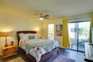 A bedroom with a bed, bedside lamps, a ceiling fan, a window with yellow curtains, and a view of the outside. - 1 Mi to the Ocean: Long Beach Condo w/ Pool Access (Long Beach)