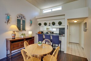 A dining area with a round wooden table, four chairs, a wooden cabinet, and a wall-mounted lamp. - 1 Mi to the Ocean: Long Beach Condo w/ Pool Access (Long Beach)