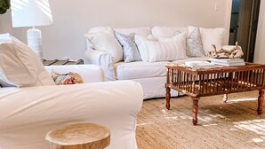 A living room with a white sofa, a wooden coffee table, and a small wooden stool. - Charming Cottage Downtown Hattiesburg (Hattiesburg)