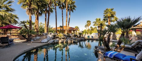 A pool area with palm trees, lounge chairs, and a building in the background.