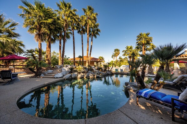 A pool area with palm trees, lounge chairs, and a building in the background.