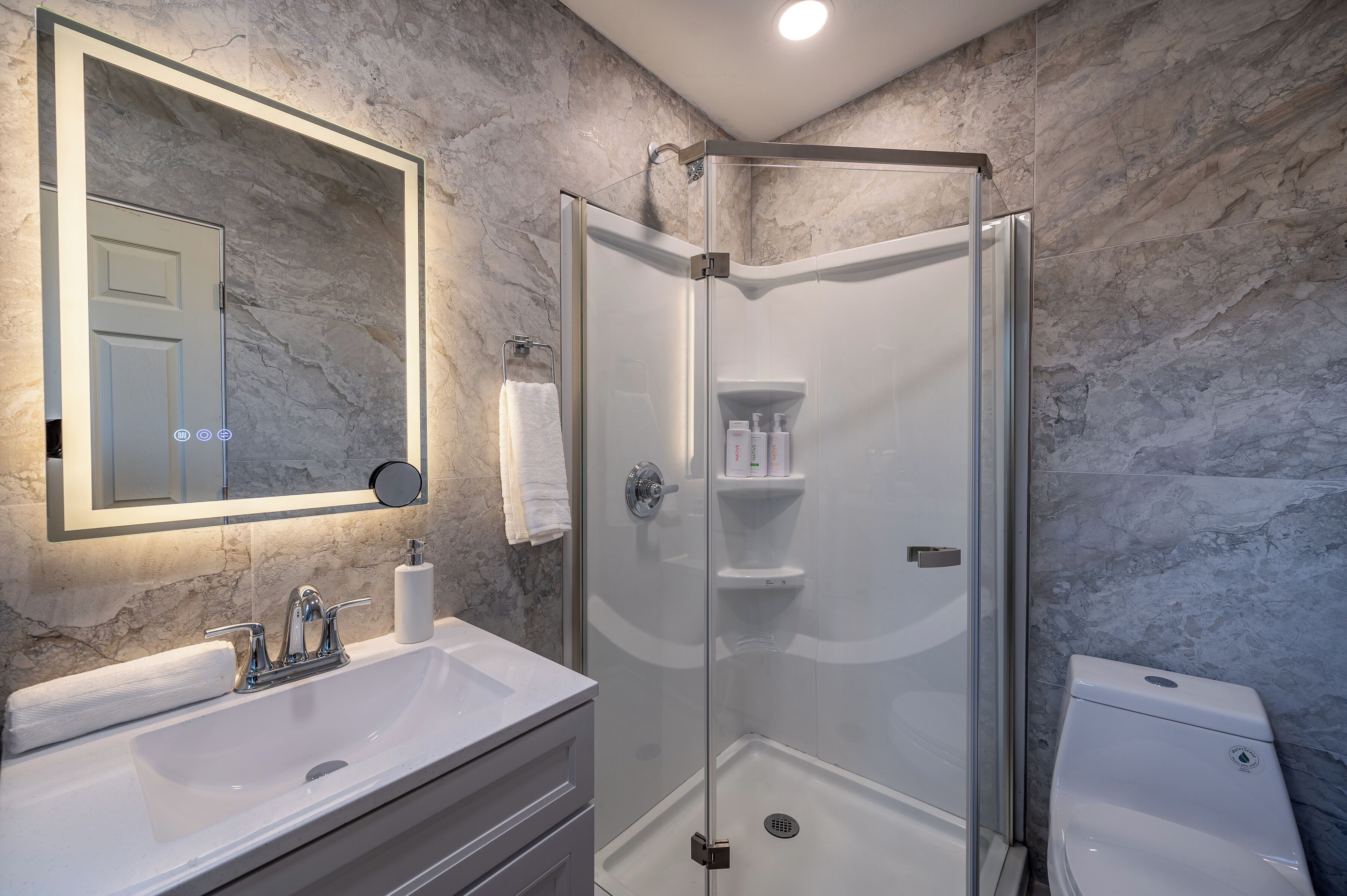A modern bathroom with a glass-enclosed shower, a white sink, and a marble wall.