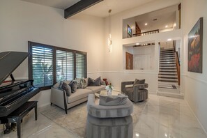 A spacious living room with a grand piano, a sofa set, a coffee table, and a staircase leading to an upper level.