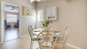 Ein Essbereich mit einem runden Tisch, weißen Stühlen, einem Deckenventilator und einem Bild an der Wand.