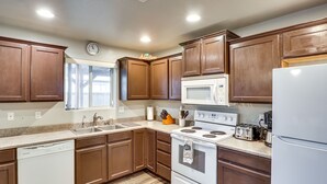 A kitchen with brown cabinets, a white dishwasher, a stove, a microwave, and a refrigerator. - Fire Pit + Covered Patio: Bullhead City Escape! (Bullhead City)
