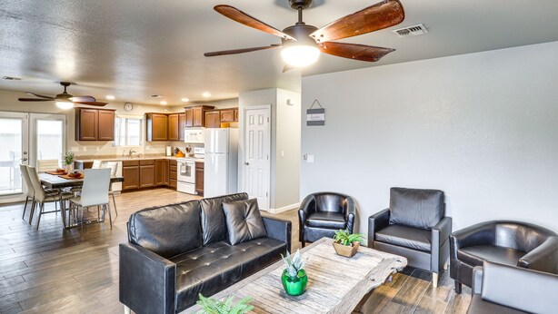 A modern living room with a black leather sofa, two leather armchairs, a wooden coffee table with plants, and a ceiling fan. - Fire Pit + Covered Patio: Bullhead City Escape! (Bullhead City)