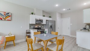 Een moderne keuken met witte kasten, een eettafel met stoelen en een bijzettafeltje.