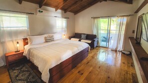 A bedroom with a large bed, wooden flooring, a ceiling fan, and a sliding glass door leading to an outdoor area.