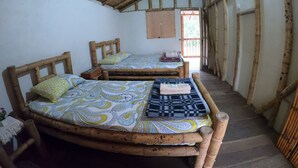 A room with two wooden beds, a window, and a bamboo ceiling.