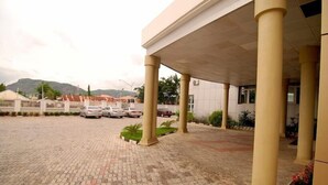 A paved courtyard with columns, a covered walkway, and parked cars. - Grand Palazzo Hotel (Abuja)