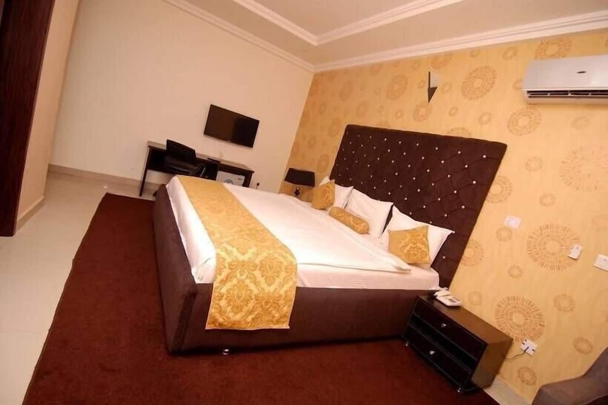 Quarto de hotel com uma cama grande, uma escrivaninha com cadeira, uma televisão de tela plana e um aparelho de ar condicionado na parede.
