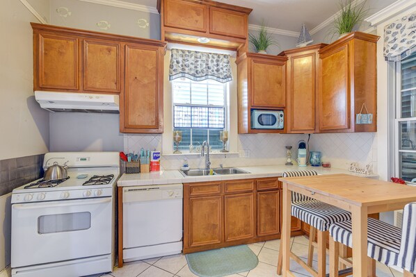 A kitchen with wooden cabinets, a white stove, a dishwasher, a microwave, a sink, and a dining table with striped chairs. - 1 Mi to Beach! Coastal Couples Escape in Galveston (Galveston)