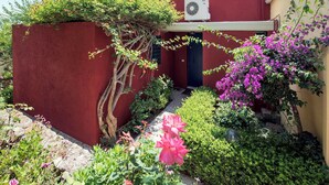 Ein rotes Gebäude mit kleinem Garten, einer Tür und einer Klimaanlage.