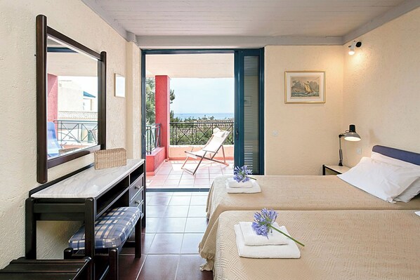 A hotel room with a bed, a bench, a desk, a chair, and a balcony with a view of the sea.
