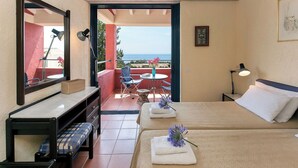 Ein Hotelzimmer mit Bett, Schreibtisch, Stuhl, kleinem Tisch und einem Balkon mit Meerblick.