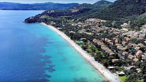 Luftaufnahme einer Küstenstadt mit Strand, Häusern und einem Bergpanorama.